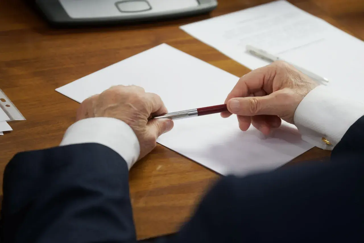 Un homme en costume tient un stylo au-dessus d'une feuille blanche, prêt à signer des documents concernant les frais de succession notaire.