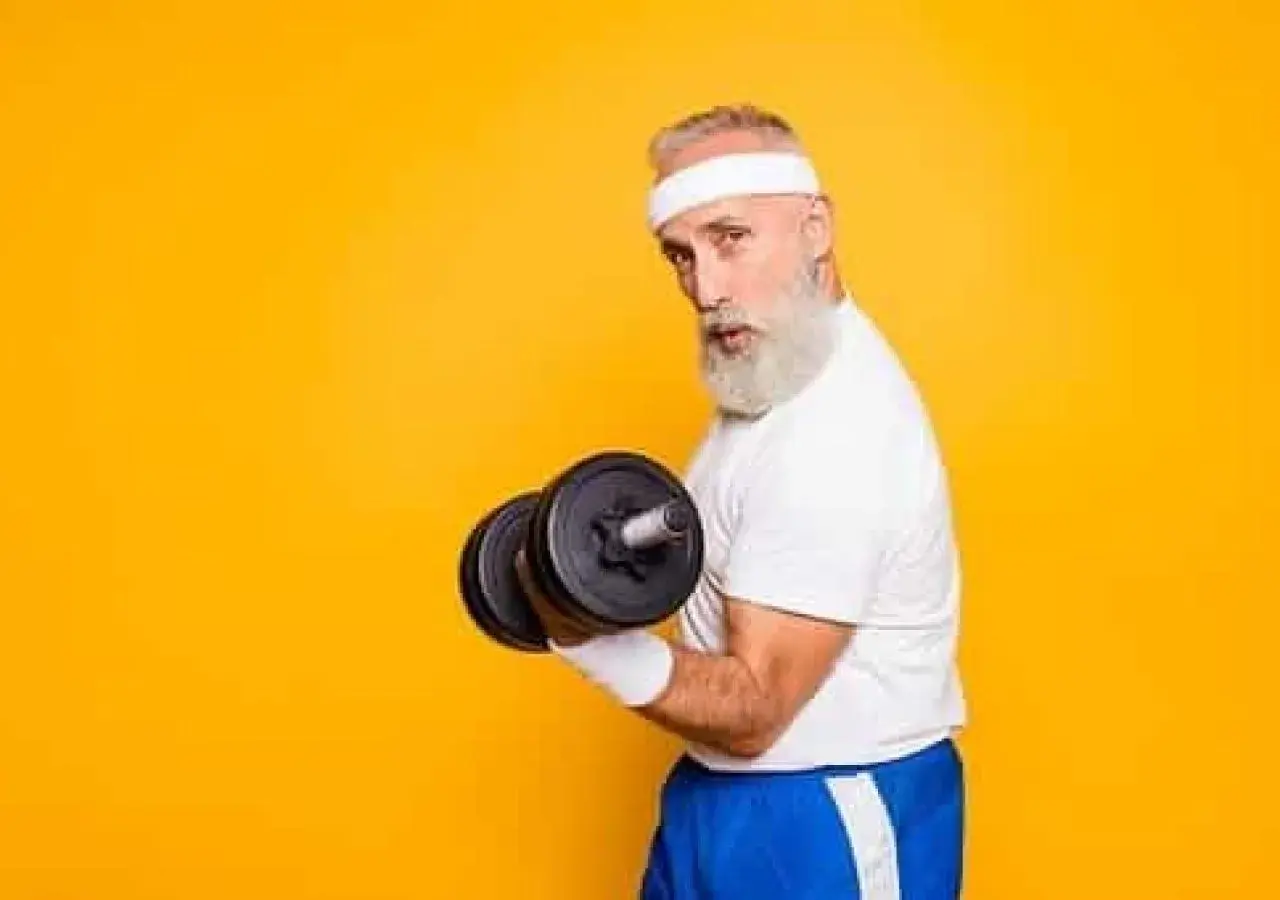 Un homme âgé avec une barbe blanche et un bandeau blanc soulève un haltère, montrant ses muscle bras.