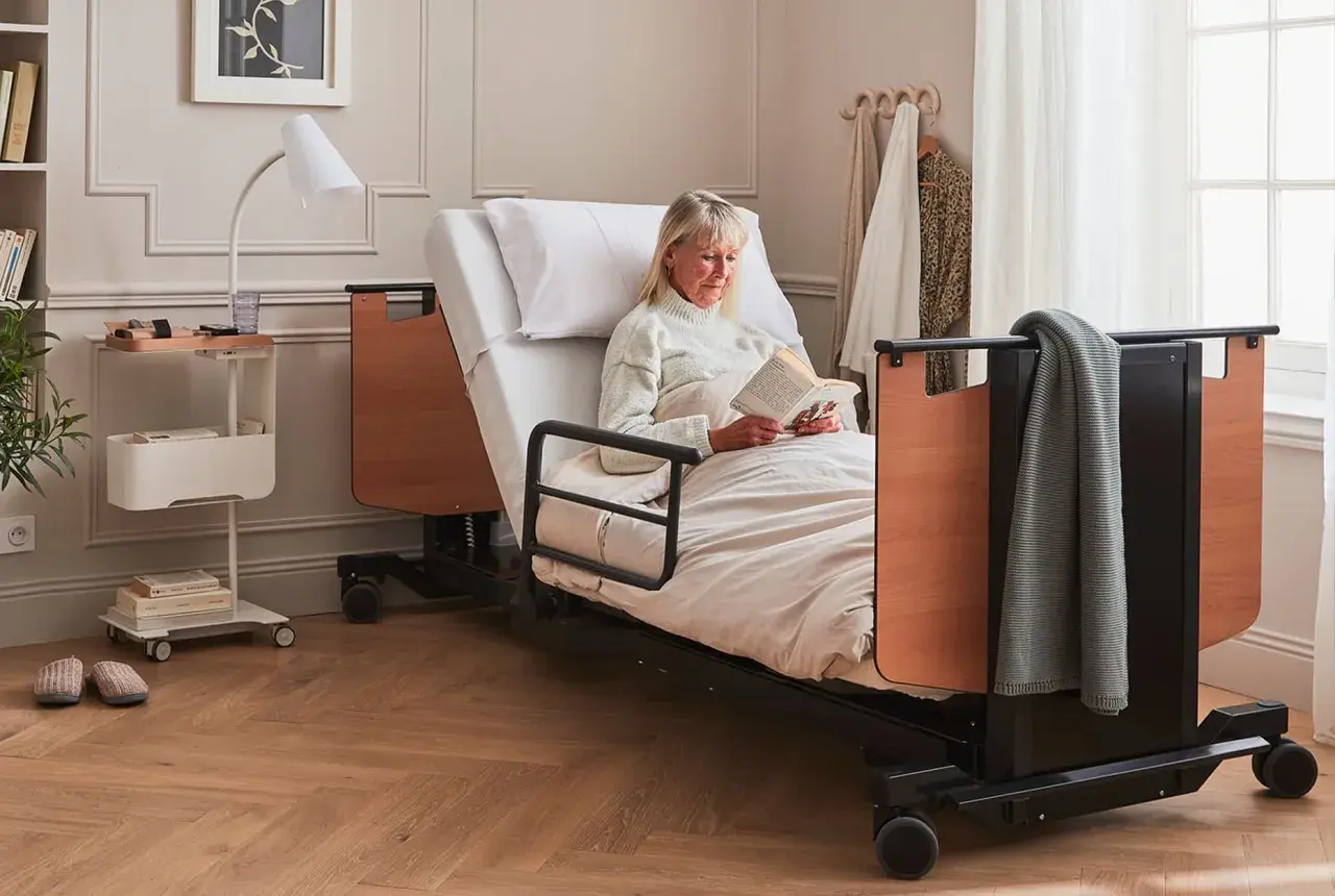 Une femme lit dans un lit médicalisé. Ce type de table de lit médicalisé est souvent éligible au remboursement de la Sécurité Sociale.