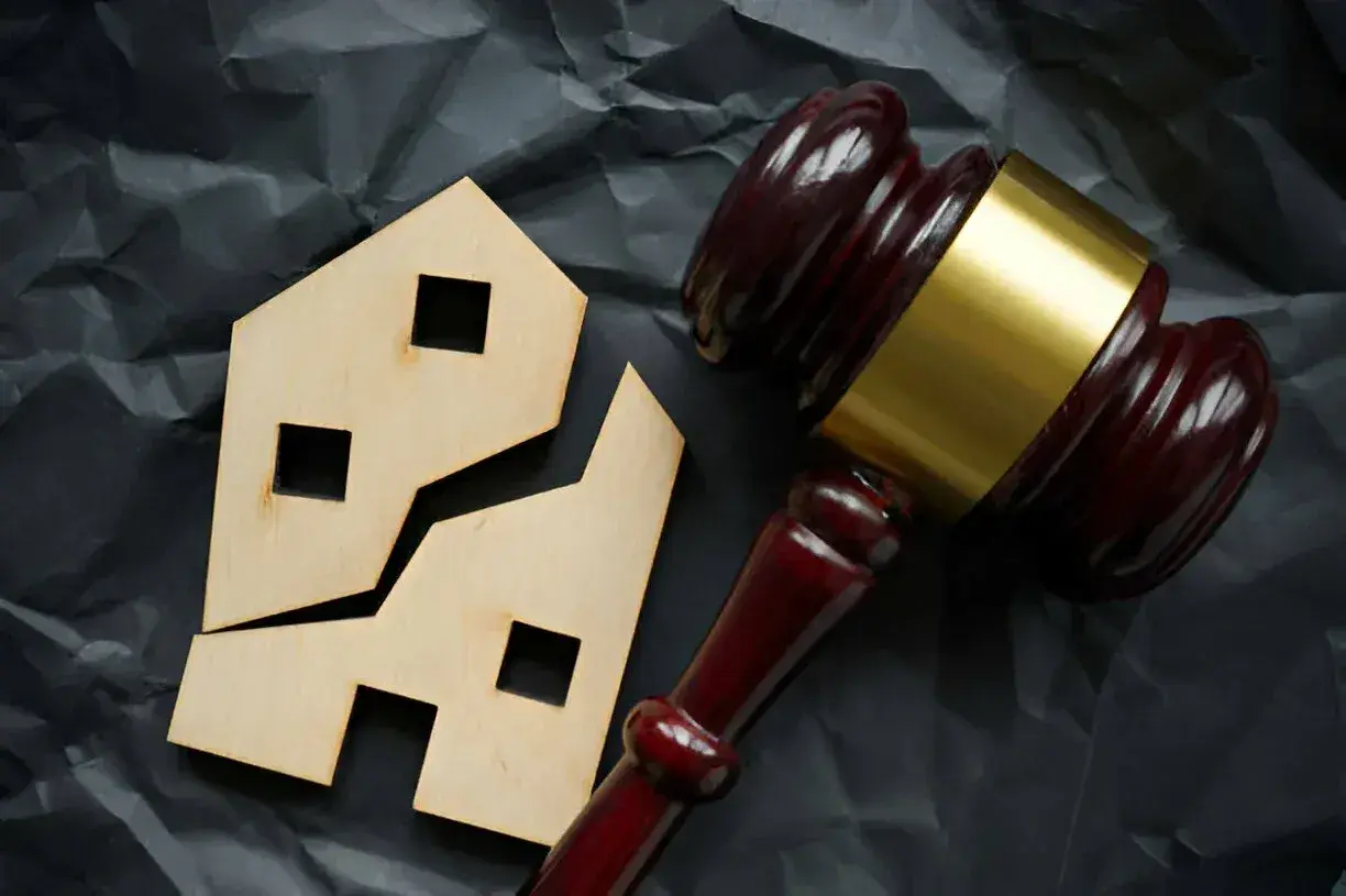 Marteau de juge près d'une maison en bois brisée. Comment éviter les droits de succession sur un bien immobilier.
