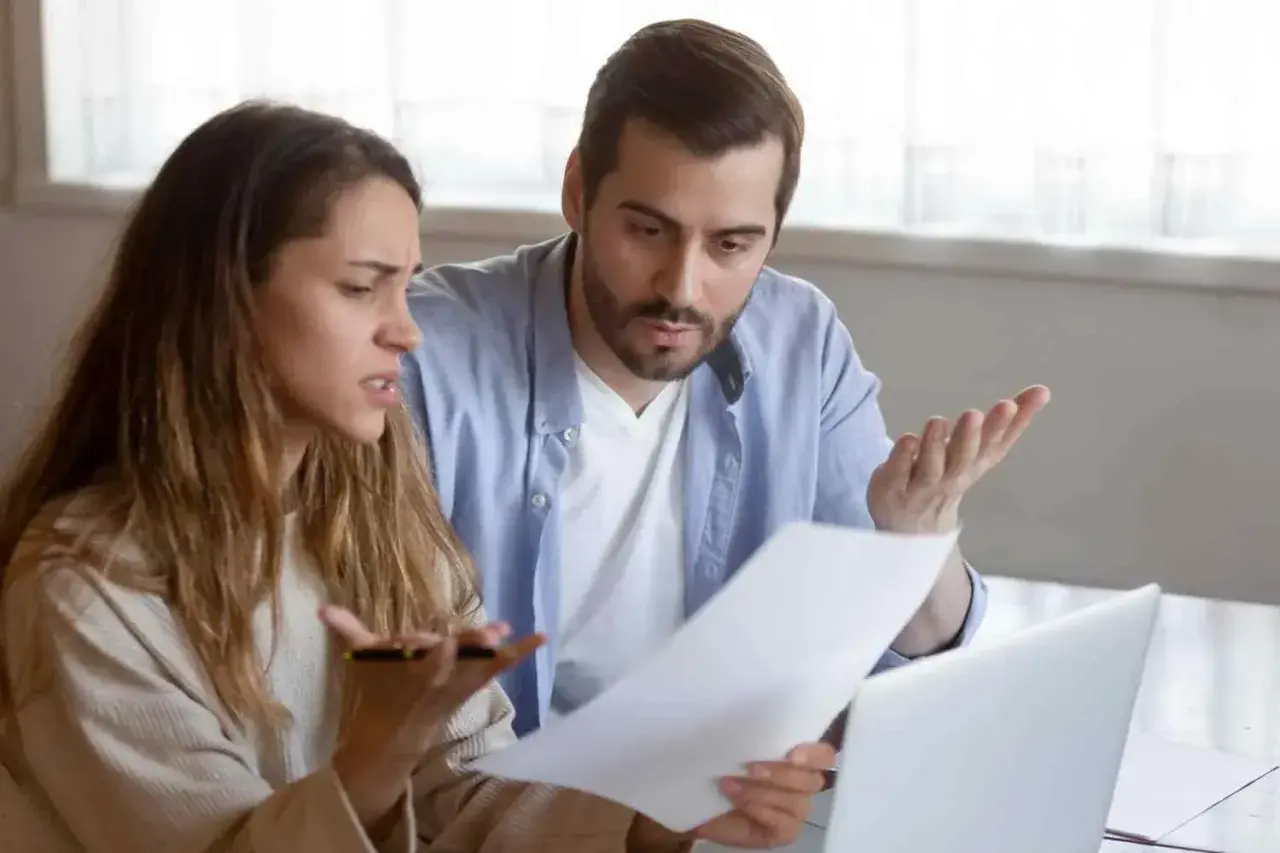 Un couple discute, perplexe, devant des documents. La question "faut il payer les droits de succession avant d'hériter ?" les préoccupe.
