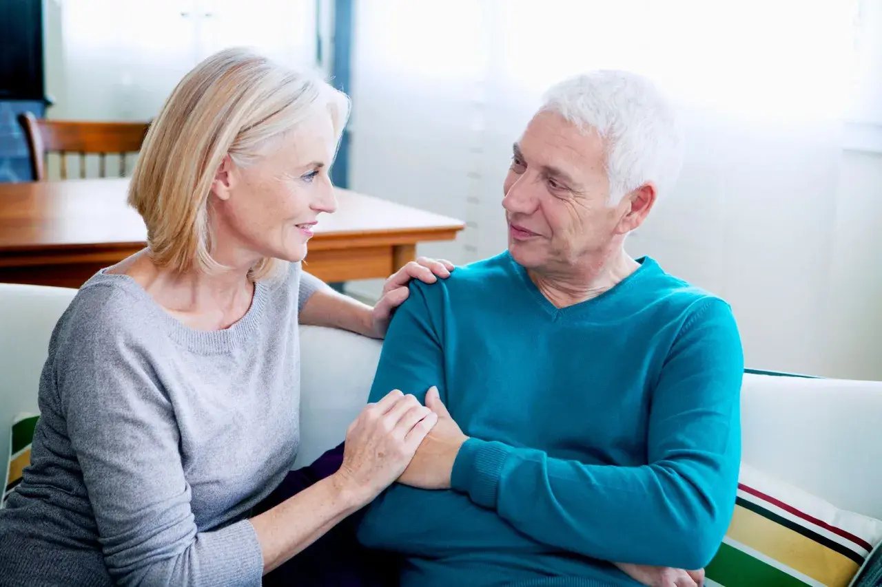 Un couple âgé discute, la femme pose sa main sur l'épaule de l'homme. Une scène qui peut évoquer les conversations difficiles, comme celles sur comment meurt-on d'un cancer du pancréas.