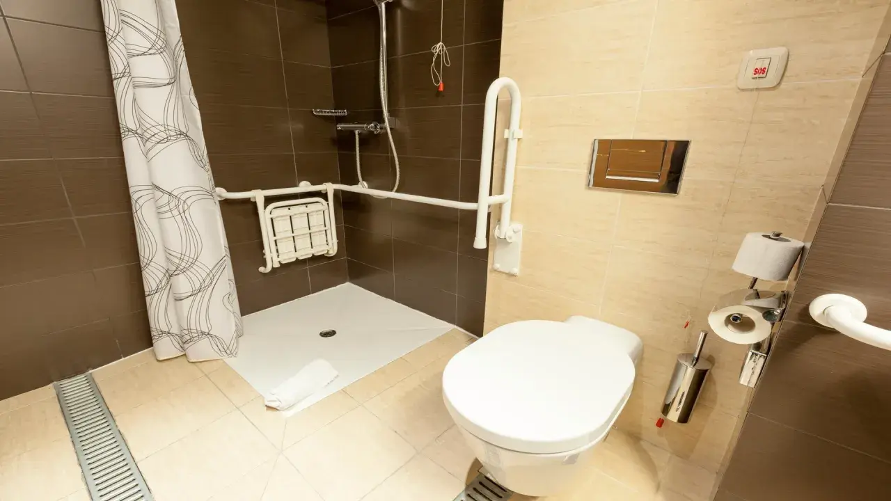 Salle de bain adaptée avec douche PMR, siège rabattable, barres d'appui et bouton d'urgence.