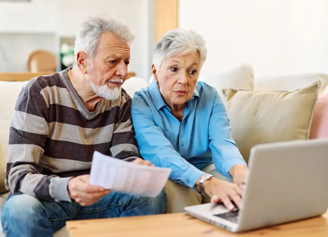 Couple âgé discutant de l'habilitation familiale et du placement en EHPAD, l'un tenant des papiers, l'autre sur un ordinateur portable.