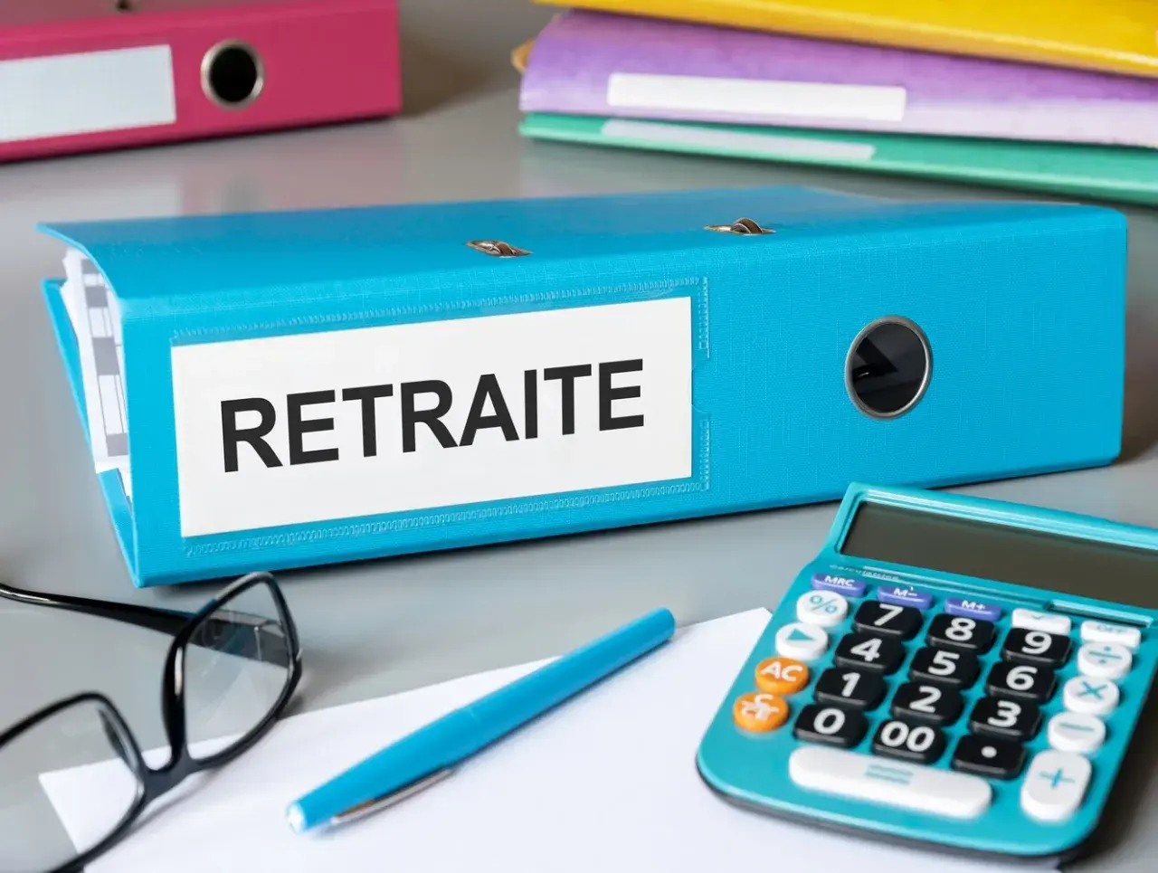 Dossier bleu "Retraite" sur un bureau, avec une calculatrice, des lunettes et un stylo. L'aspa montant est peut-être dans ce dossier.