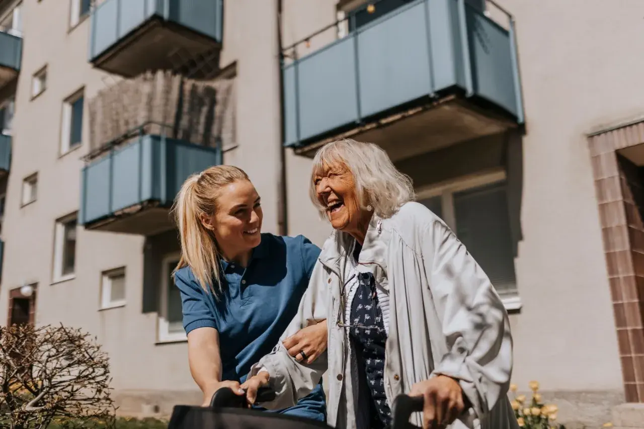 Une aide-soignante soutient une femme âgée riant aux éclats, une scène de vie chaleureuse qui pourrait inspirer une alternative maison de retraite.