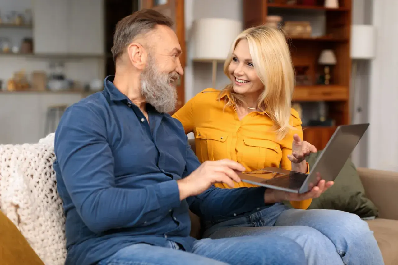 Couple souriant regardant un ordinateur portable, peut-être pour trouver de l'aide financière pour la maladie d'Alzheimer.