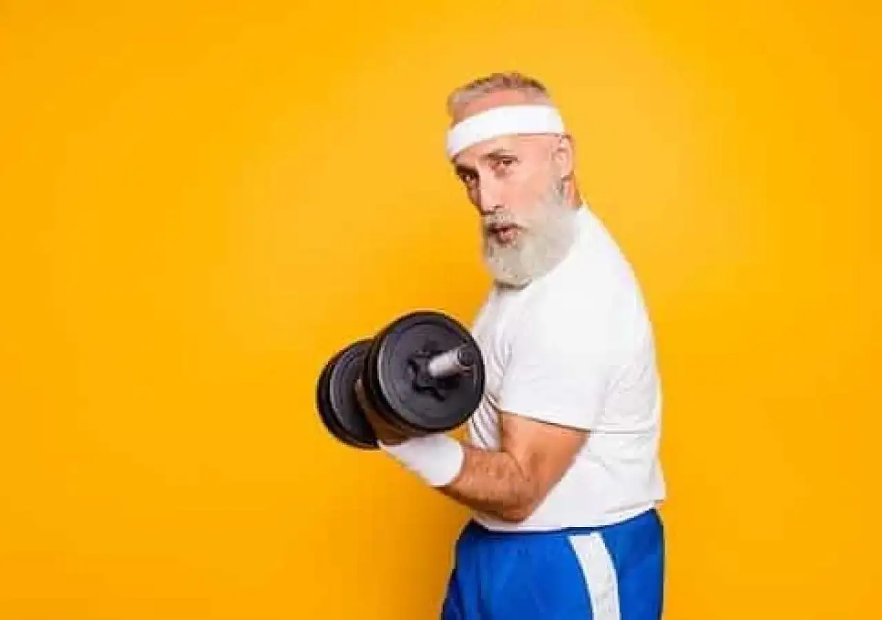 Un homme âgé avec une barbe blanche et un bandeau blanc soulève un haltère, montrant ses muscle bras.