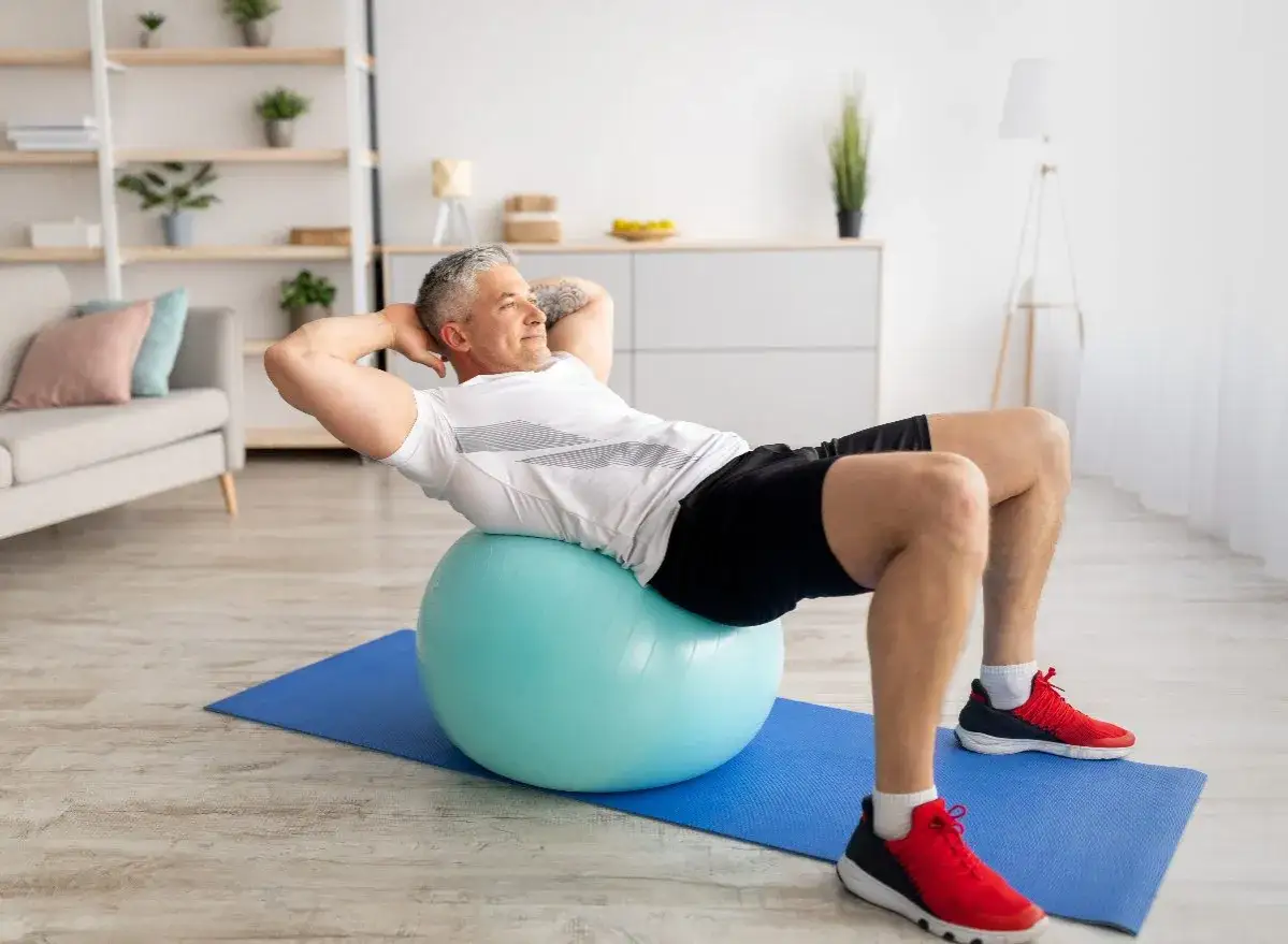 Homme faisant un exercice swiss ball pour renforcer ses abdominaux, confortablement install&eacute; chez lui.