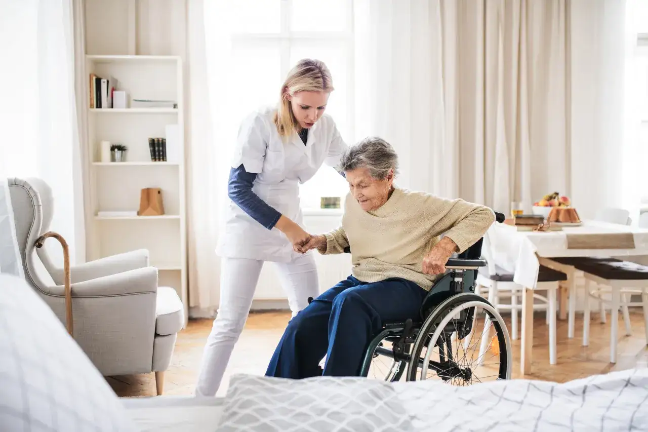 Une aide-soignante aide une femme &acirc;g&eacute;e en fauteuil roulant &agrave; se lever. Une belle journ&eacute;e pour sortir plus, sans se soucier du tarif.