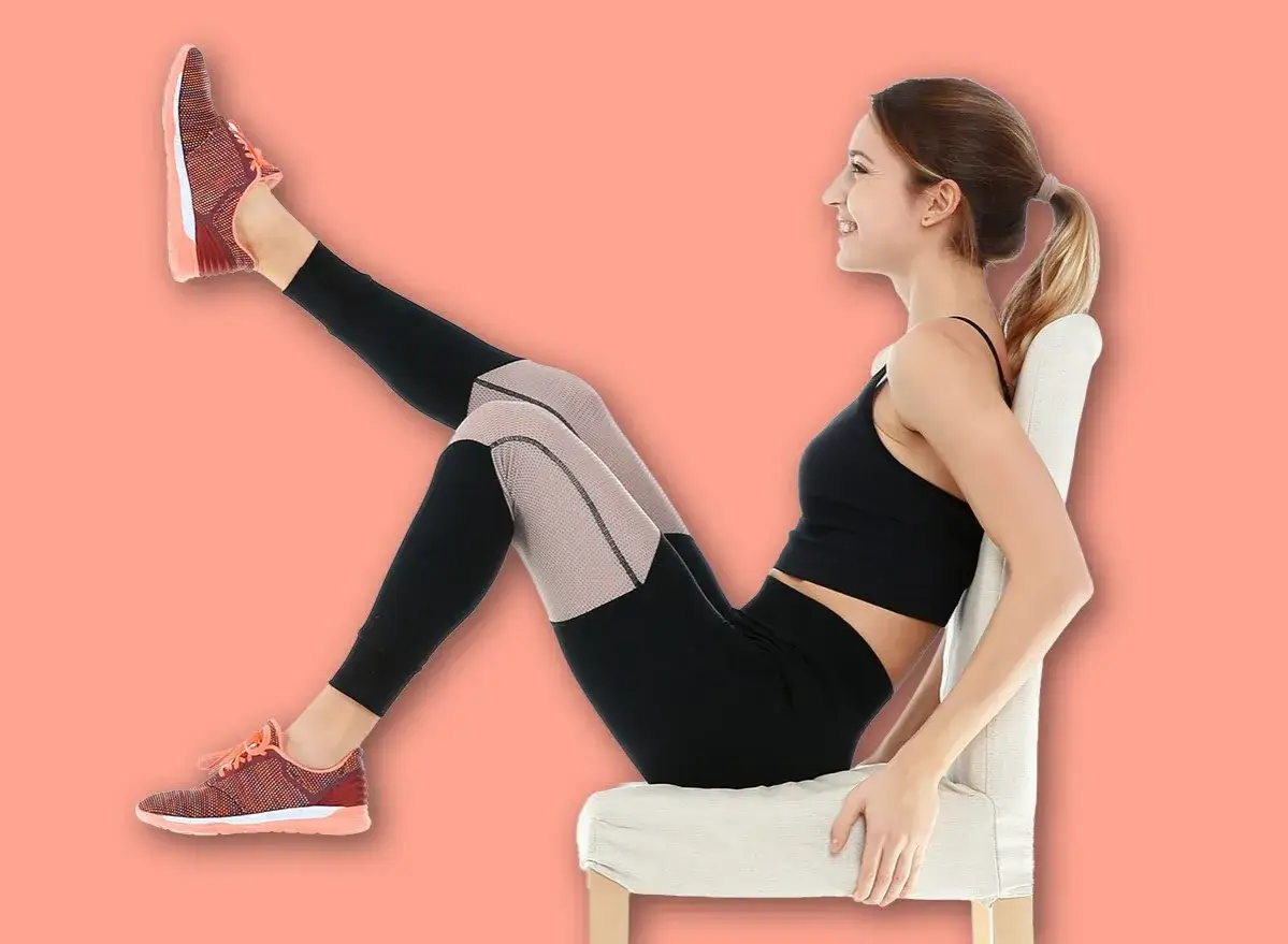 Femme souriante faisant un exercice pour comment muscler ses cuisses apr&egrave;s 60 ans, assise sur une chaise, jambe lev&eacute;e.