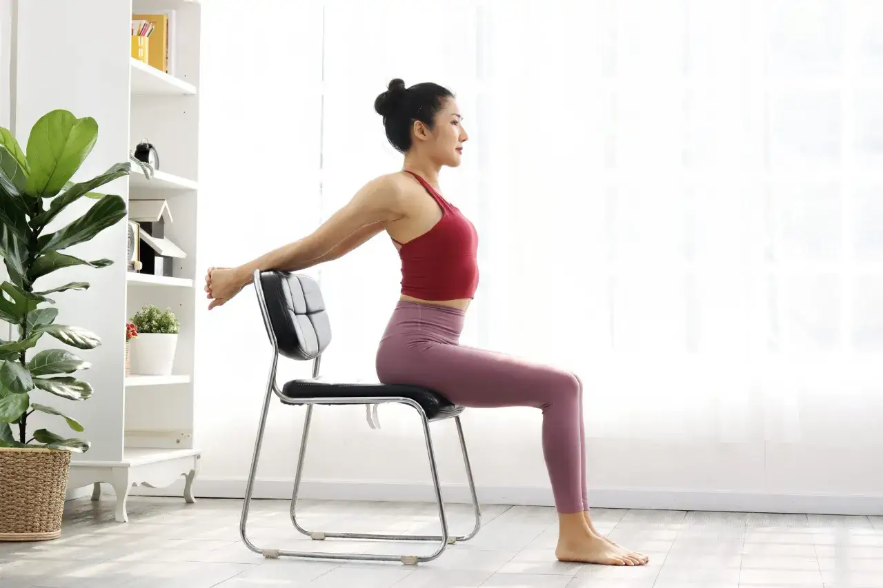 Femme pratiquant la gym douce Pilates, assise sur une chaise, bras derri&egrave;re la t&ecirc;te pour un &eacute;tirement.