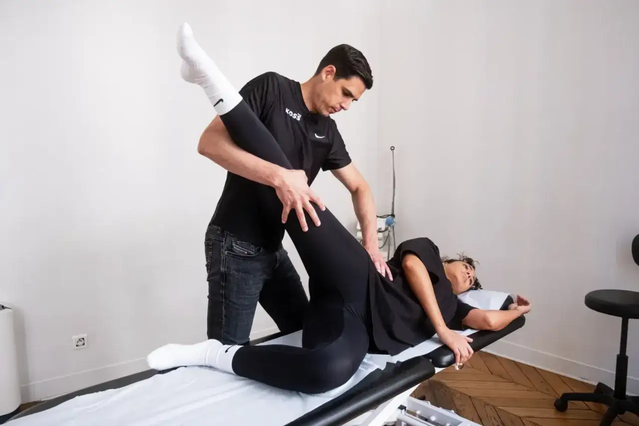Un kinésithérapeute aide une patiente à réaliser un exercice kiné hanche, en soulevant doucement sa jambe levée.