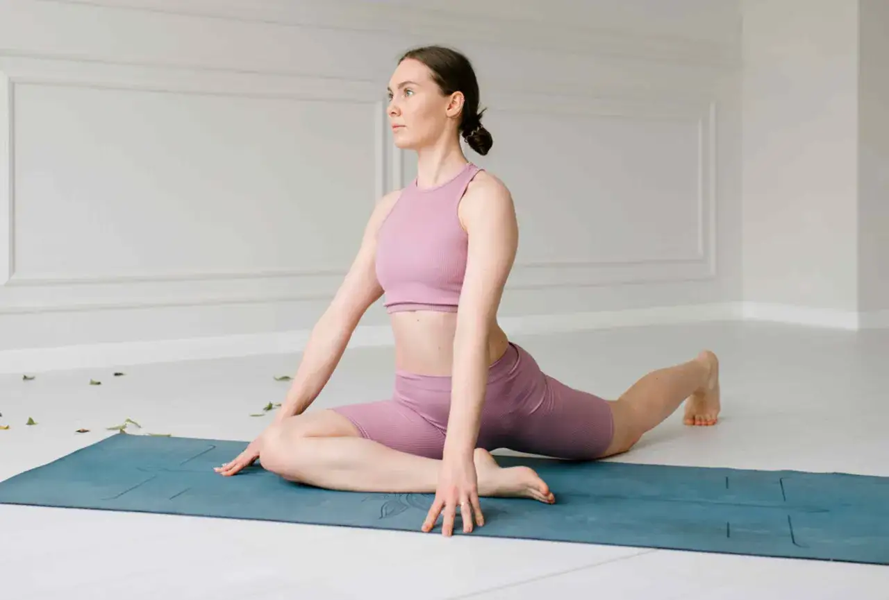 Une femme souple, même à 50 ans, fait le grand écart sur un tapis de yoga bleu, démontrant sa flexibilité et sa force.