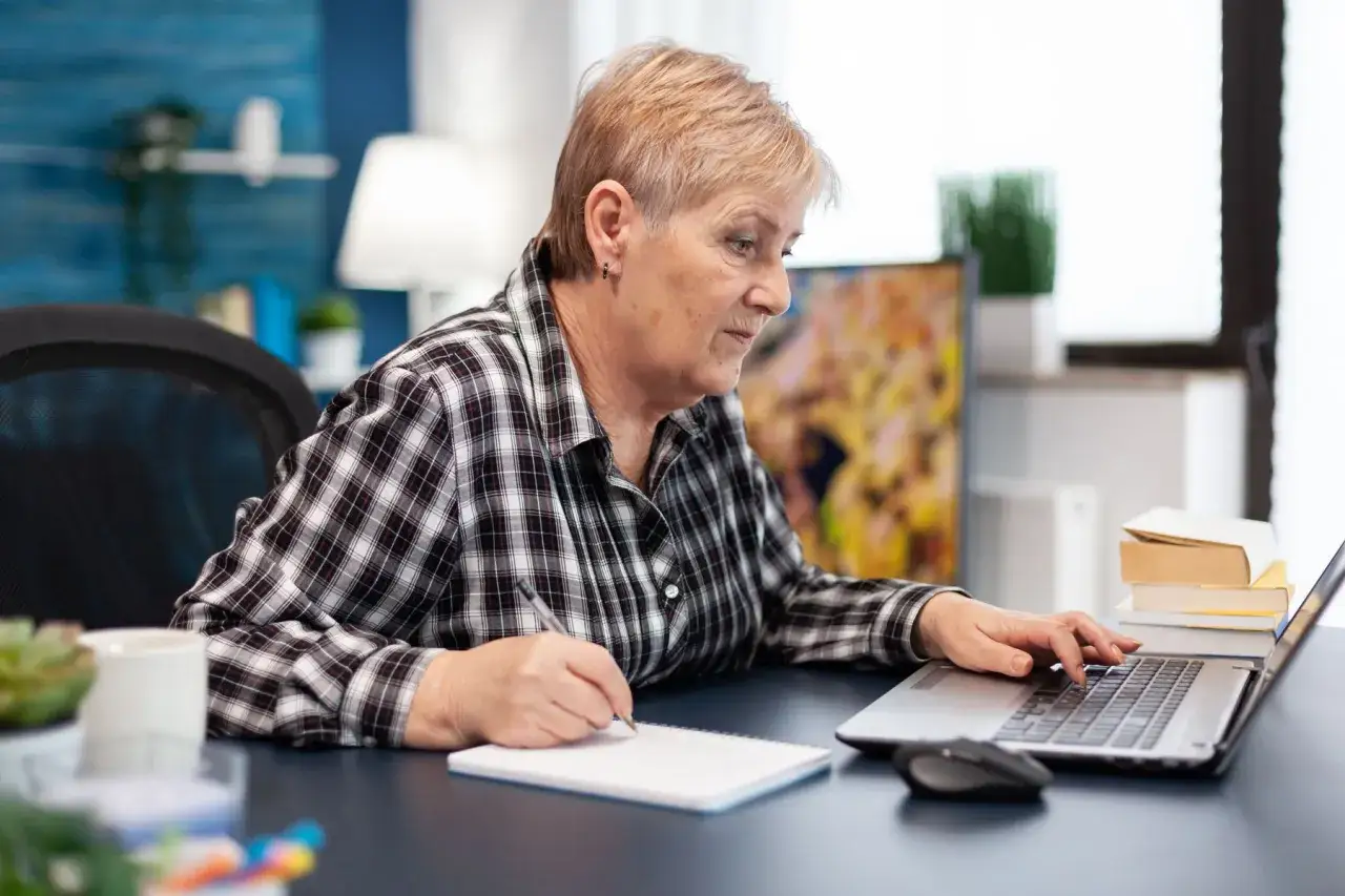 Femme âgée travaillant sur son ordinateur portable, prenant des notes pour le montant APL en EHPAD.
