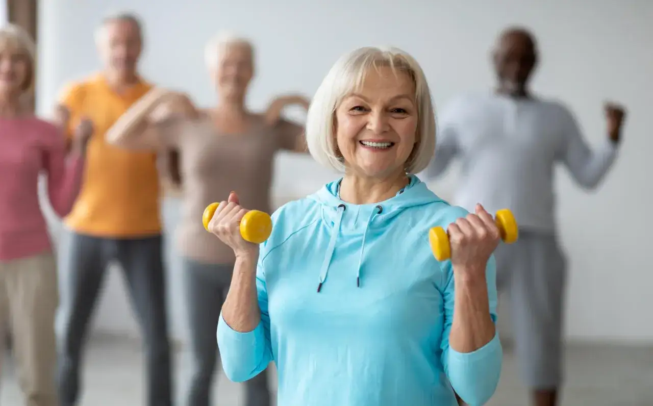 Un groupe de seniors souriants fait du sport &agrave; la maison avec des halt&egrave;res jaunes.