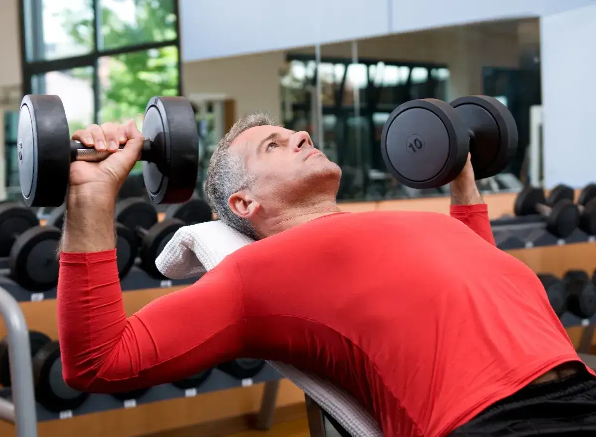 Un homme 50 ans muscl&eacute;, concentr&eacute;, soul&egrave;ve des halt&egrave;res sur un banc de musculation.