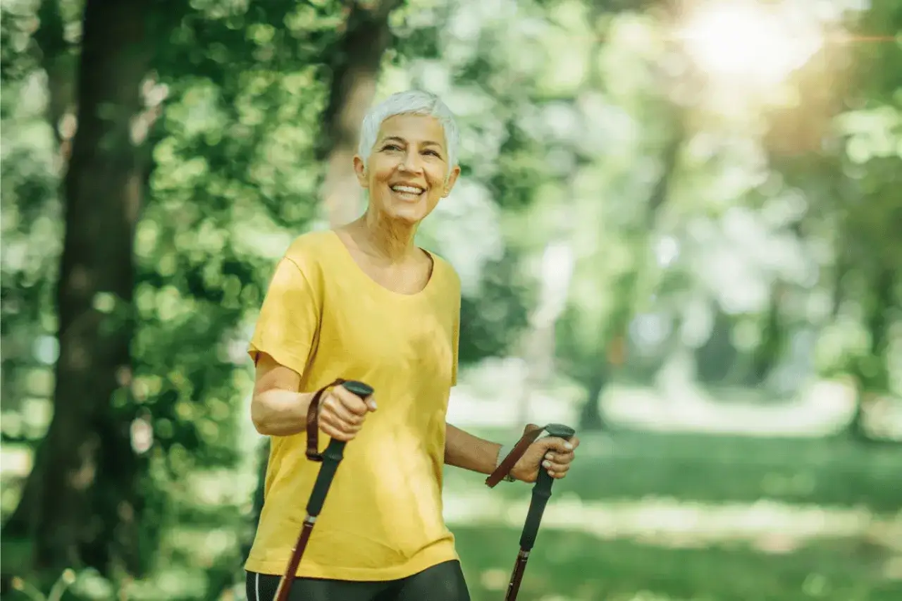 Une femme souriante profite de la vitesse marche nordique dans un parc ensoleillé.