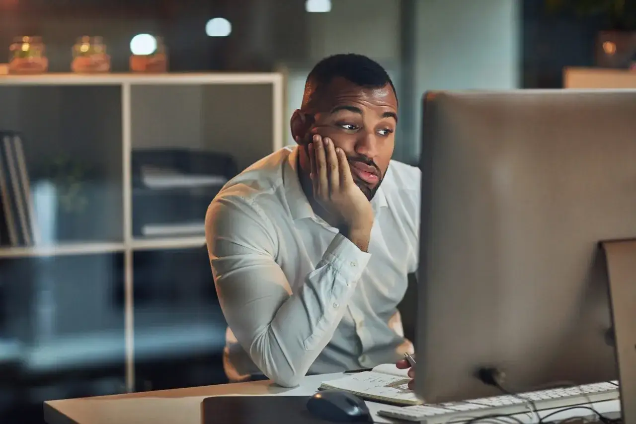 Un homme d'affaires, le visage appuy&eacute; sur la main, semble souffrir d'un coup de fatigue dans la journ&eacute;e, regardant son &eacute;cran d'ordinateur avec lassitude.