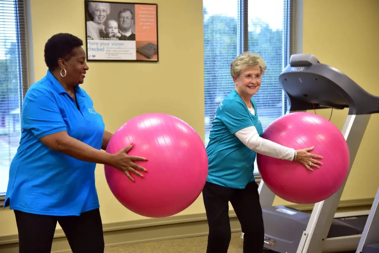 Deux femmes souriantes font du sport avec des ballons roses. L'une d'elles porte un t-shirt bleu, l'autre un t-shirt turquoise. Elles semblent s'entraîner pour lutter contre l'hypothyroïdie.