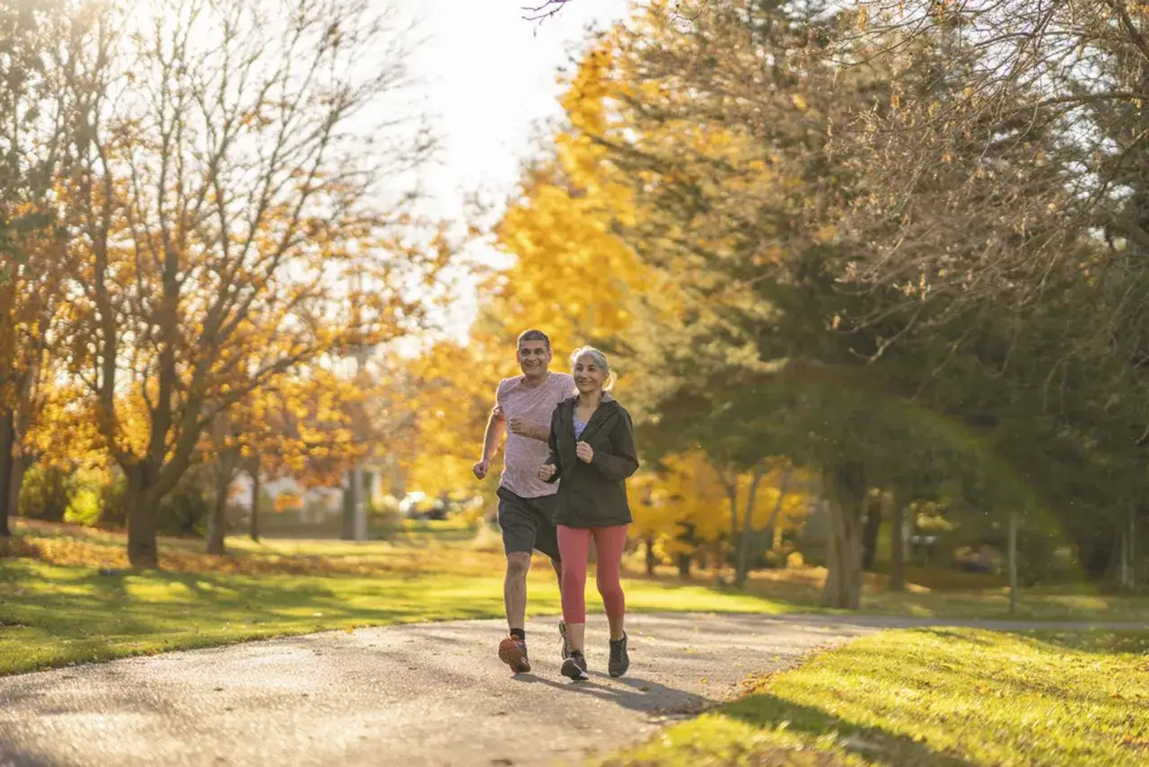 Couple souriant courant dans un parc en automne, profitant de l'air frais et augmentant leur nombre de pas par jour.