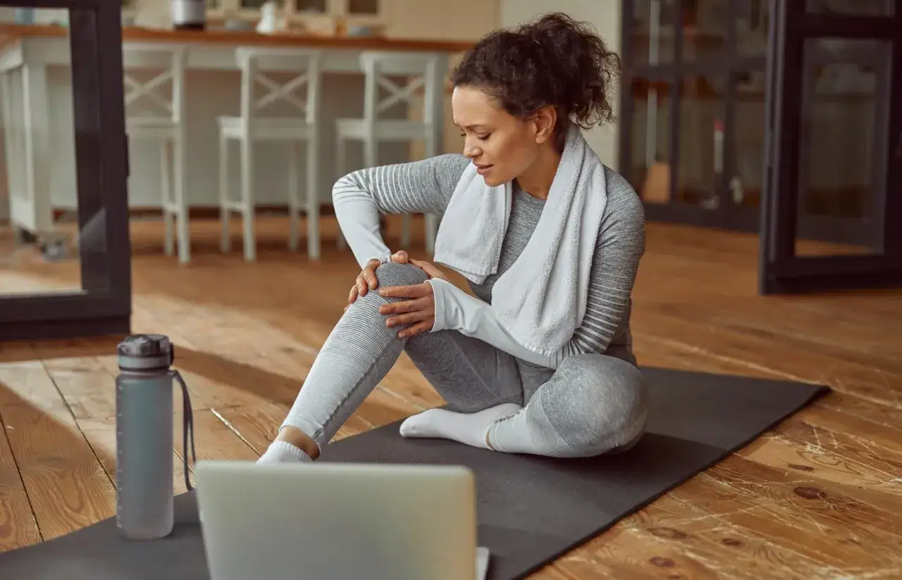 Femme assise sur un tapis de yoga, tenant son genou douloureux.