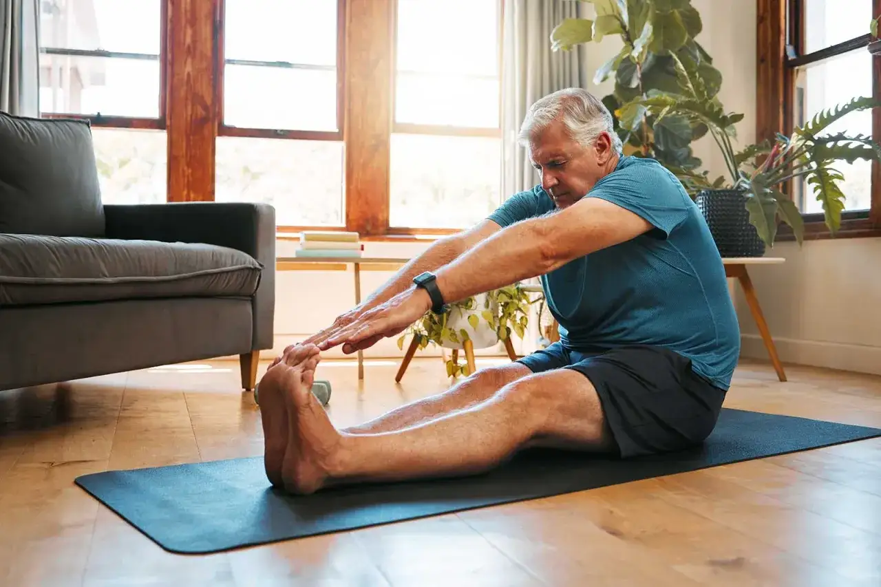 Un homme de 70 ans fait des étirements sur un tapis, un exemple de gym pour seniors 70 ans.