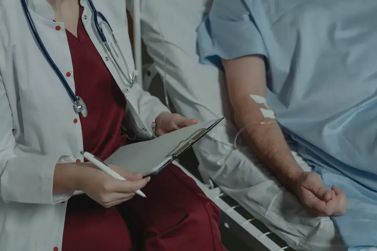 M&eacute;decin consultant un dossier pr&egrave;s d'un patient sous perfusion, &eacute;voquant le parcours difficile du comment meurt-on d'un cancer du pancr&eacute;as.