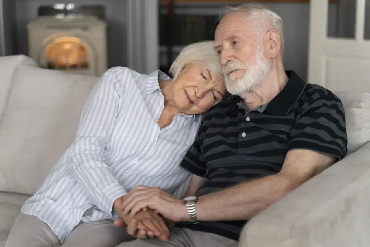 Un couple &acirc;g&eacute; se repose sur un canap&eacute;, la femme s'appuyant sur l'&eacute;paule de son mari. Une sc&egrave;ne touchante qui &eacute;voque le besoin d'aide pour EHPAD Alzheimer.