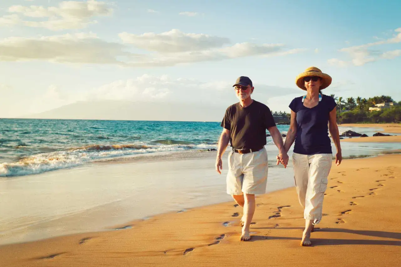 Couple senior main dans la main sur la plage, profitant d'un village paisible au bord de la mer.