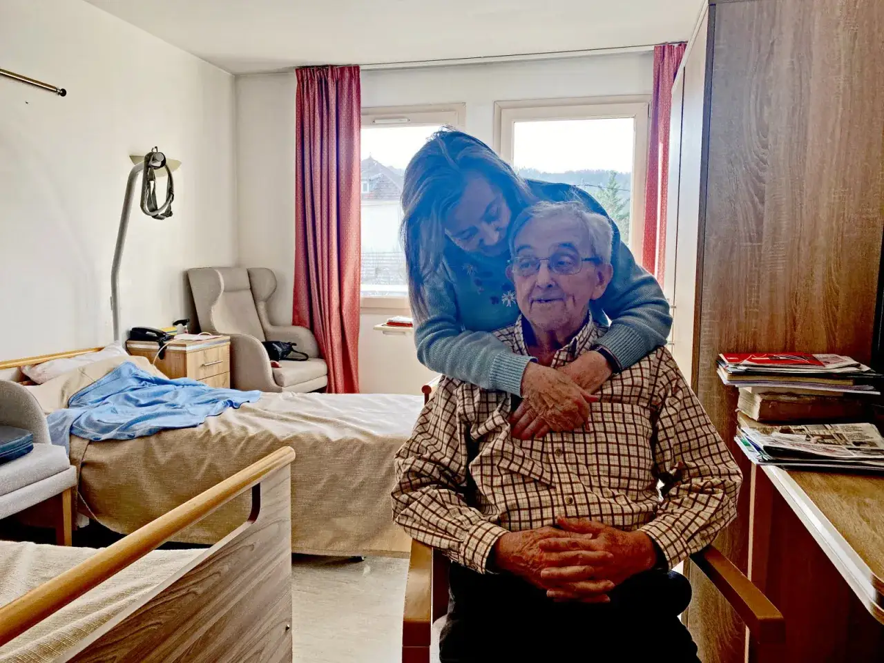 Une femme enlace tendrement un homme &acirc;g&eacute; dans une chambre d'EHPAD. Le tarif EHPAD pour un couple est une pr&eacute;occupation, mais l'amour familial est inestimable.