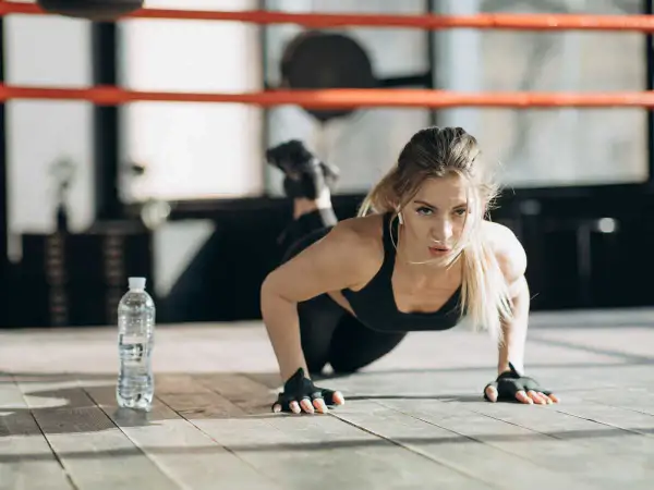 Femme faisant des pompes, un excellent exercice pour bras fripés. Elle est concentrée, dans une salle de sport.