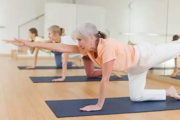 Trois femmes pratiquent un exercice jambe en équilibre sur un tapis de yoga.