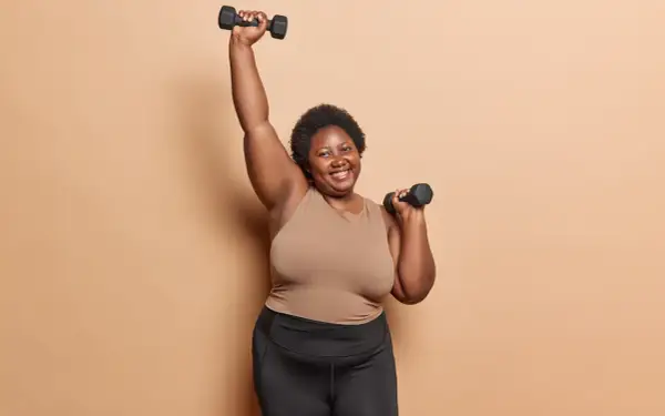 Femme souriante faisant des charges pour musculation à 70 ans, bras levés avec des haltères.