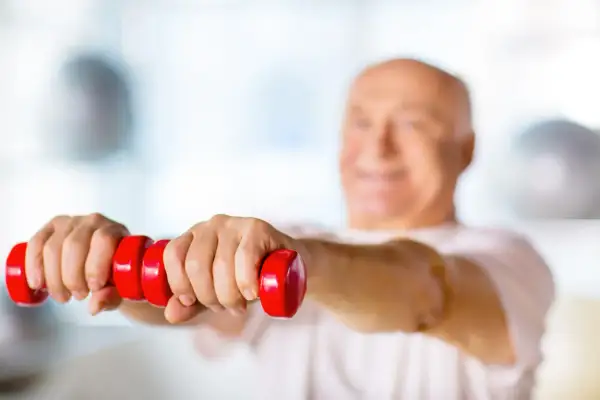 Un homme souriant, la soixantaine bien entamée, fait des exercices avec des haltères rouges. Un exemple de gym pour seniors 70 ans.