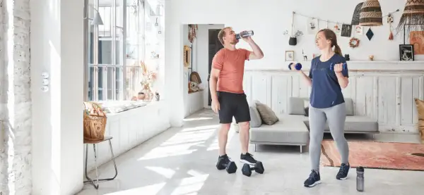 Un homme boit de l'eau pendant que sa compagne fait des exercices avec des haltères, développant ses muscles du bras.