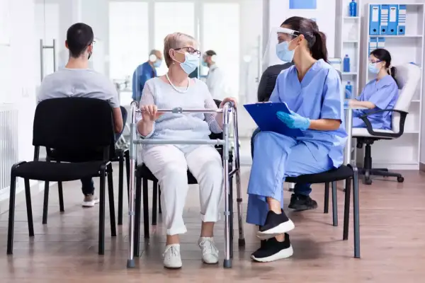 Une patiente âgée avec un déambulateur discute avec une infirmière masquée dans une salle d'attente d'un usld hôpital.