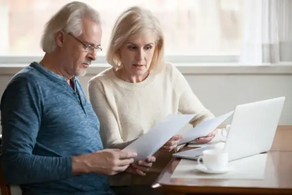 Couple âgé examine des documents, espérant une augmentation aah de 1000 euros. Ils semblent concentrés sur leurs finances.