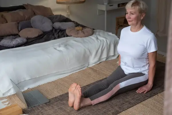 Femme de 60 ans s'entraînant à la maison pour comment muscler ses cuisses après 60 ans, suivant une vidéo sur son ordinateur portable.