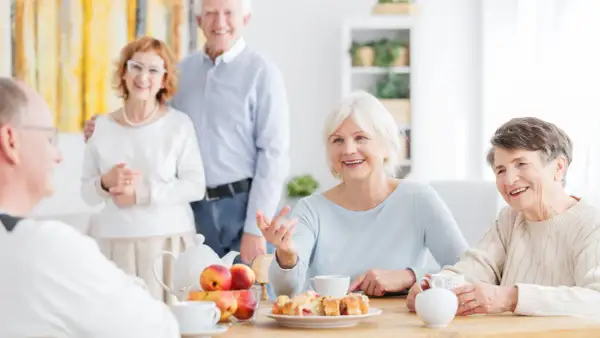 Des aînés souriants partagent un moment convivial autour d'un thé et de pâtisseries. Une définition de la marpa : un lieu de vie chaleureux pour seniors.