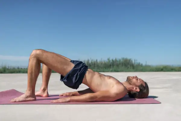 Homme en plein exercice de renforcement du plancher pelvien, allongé sur un tapis de yoga à l'extérieur.