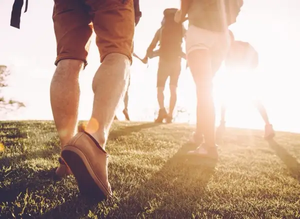 Des randonneurs marchent sur une colline herbeuse au coucher du soleil. Une façon naturelle de muscler son dos en marchant.