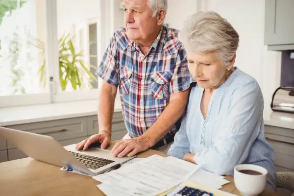 Couple âgé examinant des documents et un ordinateur portable, s'interrogeant sur combien coûte une maison de retraite.