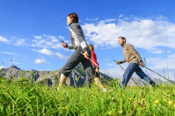 Trois personnes pratiquent la marche nordique dans un paysage montagneux, profitant de la vitesse et du grand air.