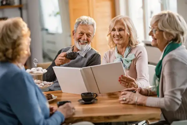 Quatre seniors souriants partagent un moment convivial autour d'un album. L'espérance de vie après entrée en EHPAD peut être belle et joyeuse.