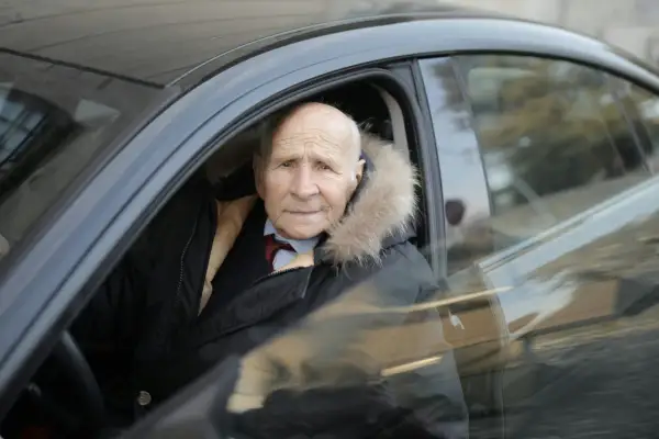 Un homme âgé, un senior à partir de quel âge, porte une veste d'hiver avec un col en fourrure, assis dans une voiture.